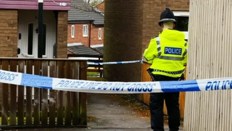 The back of a male police officer outside houses. A blue and white police cordon  is in the foreground.