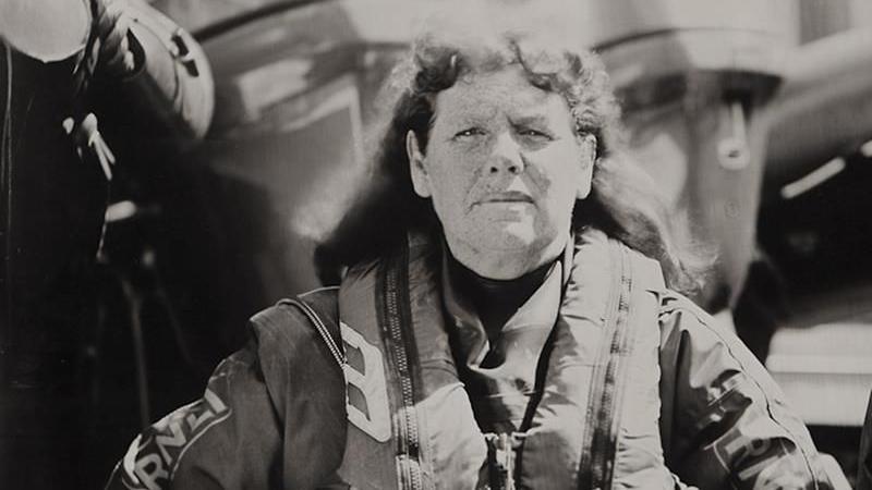 A black-and-white photo of Liz staring straight ahead and standing in front of an RNLI vessel. 