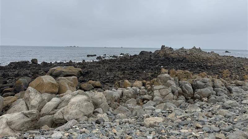 Portinfer rock pools. A landscape image of the rocks and the sea in the background. The sky is overcast. 
