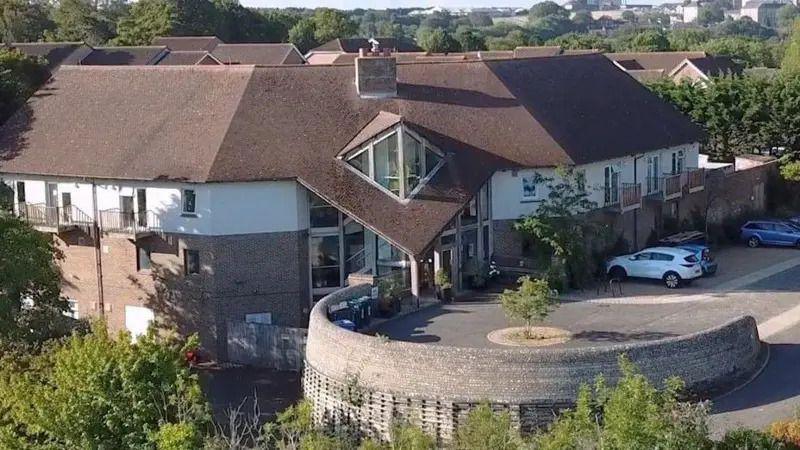 The Sussex Beacon centre. A white and brown building with a brown roof. There is a car park to the right of the building