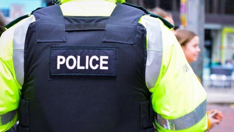 Close shot of a police officers back, wearing a black police vest on a hi-viz jacket 