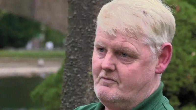 A man in his 50s with sandy hair and a green-collared shirt looks to the side of the camera.