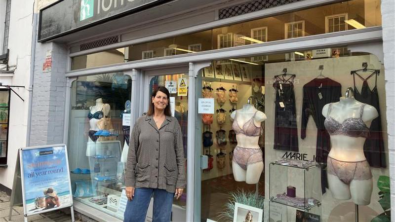 A woman stands outside a shop selling ladies' underwear. 