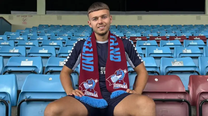 A photograph of Jonathan Gjoshe sitting in the stands while wearing a burgundy and blue scarf