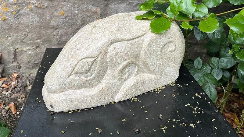 A stylised stone hare hunched over on a plinth low to the ground