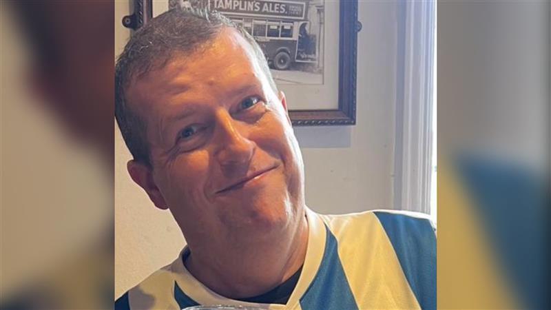 A man in a blue and white Brighton and Hove Albion shirt smiling at the camera.