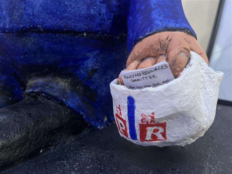 A close up on a papier mâché hand holding a shopping bag with papers 