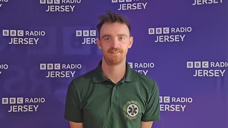 Nathan Judge stood in front of a purple BBC Radio Jersey backdrop. He is wearing a green t-shirt which has a NPA Medical badge on the right.