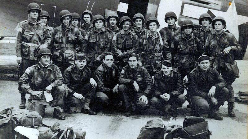 82nd airborne pose infront of a plane with bags and parachutes infront of them