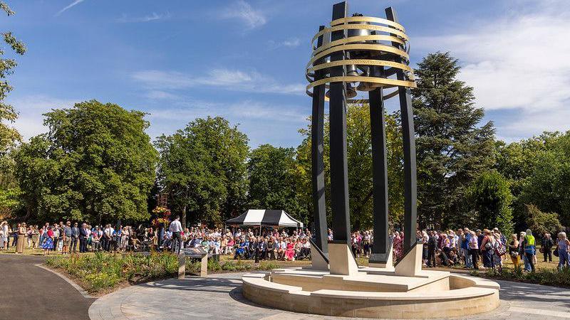 Hope Bell memory stands in front of a crowd of people sitting and standing in Queens Park, Loughborough