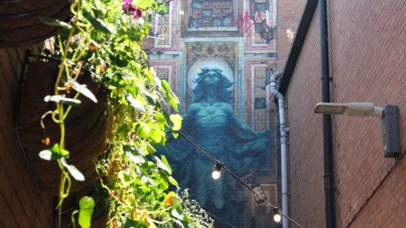 Plants hanging on a wall in front of a mural of a blue figure looking upwards