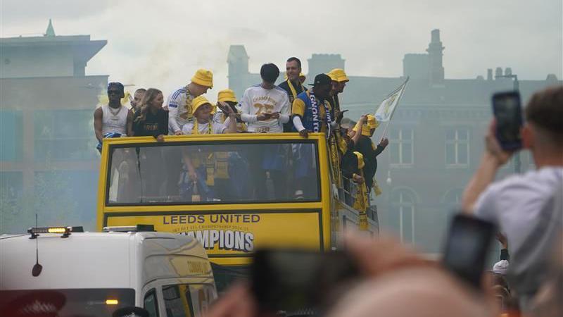 Leeds United bus rides on the road with the staff and players standing on the top deck