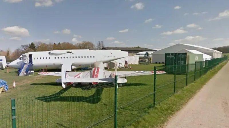 A large passenger jet and a smaller plane, possibly a mosquito, both white, stand on the grass outside a marquee at the museum. 