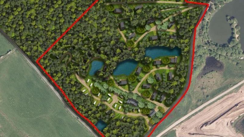 An aerial map of the proposed development which has a red boundary outlining the land. In the middle there are four lakes surrounded by trees. The roofs of lodges and caravans can also be seen. Sand is visible to the right of the development.