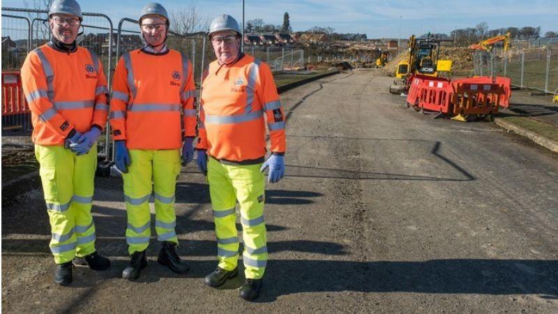 Three men stand on a road connection that is under construction