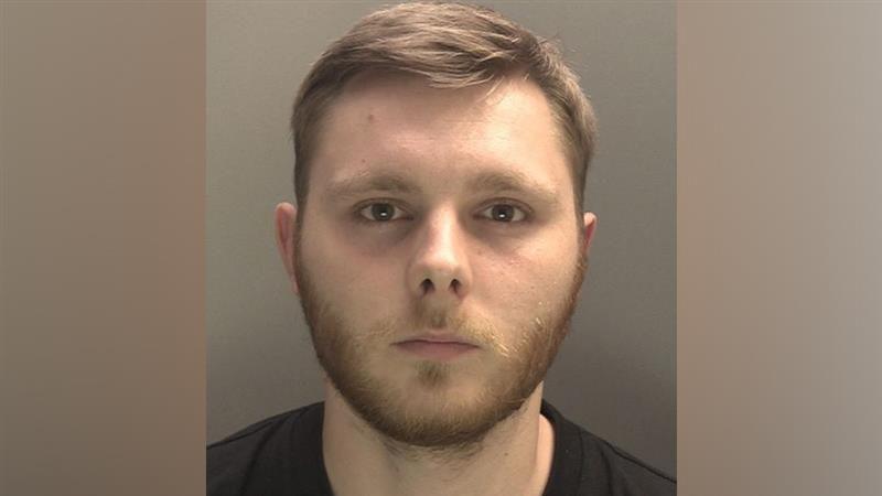 Joel Dever is pictured in a police mugshot. He has short light brown hair and a beard and is wearing a black top.