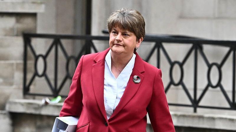 Arlene Foster pictured on her way into the NI Covid Inquiry in May 2024.  She is wearing a red suit jacket and white blouse and is holding a white folder under her arm