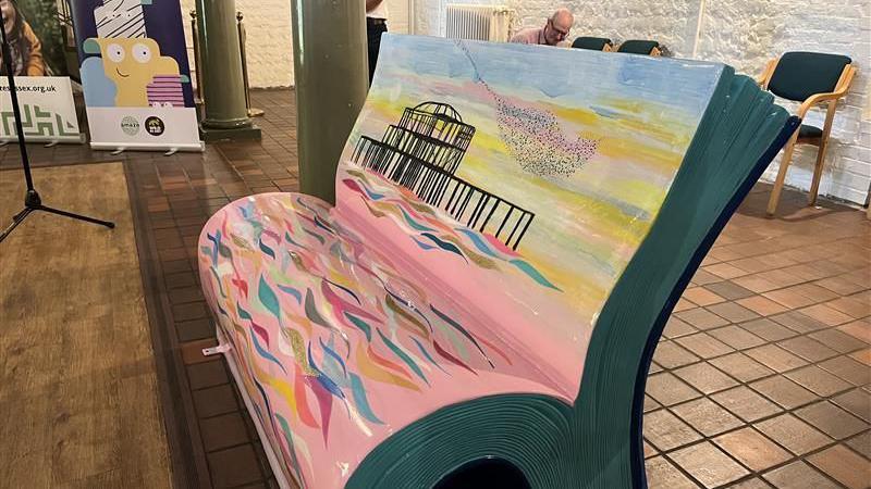 a bench which is a half open book which has the west pier on it, multi coloured waves and murmurations flying around