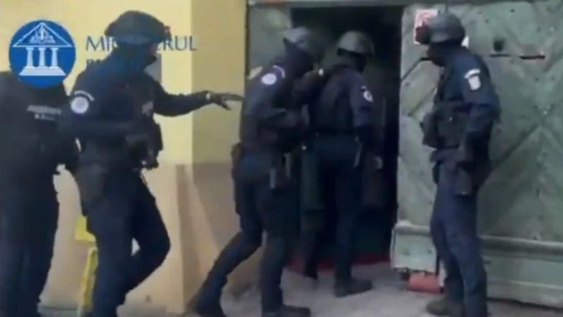 Armed Romanian police officers push down the door of a property wearing heavy protective gear.