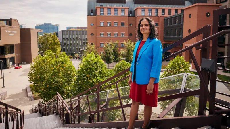 Paik seen smiling on top of a staircase with university buildings in the background