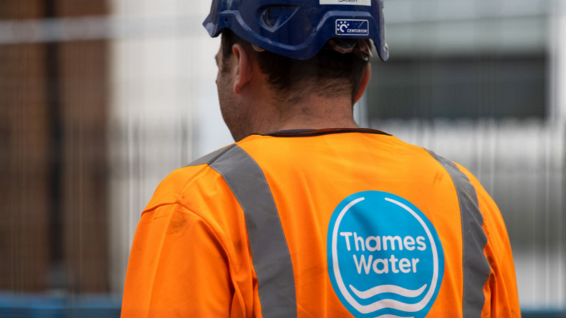 The back of a Thames Water worker who is wearing an orange hi-vis top with a blue construction hard hat