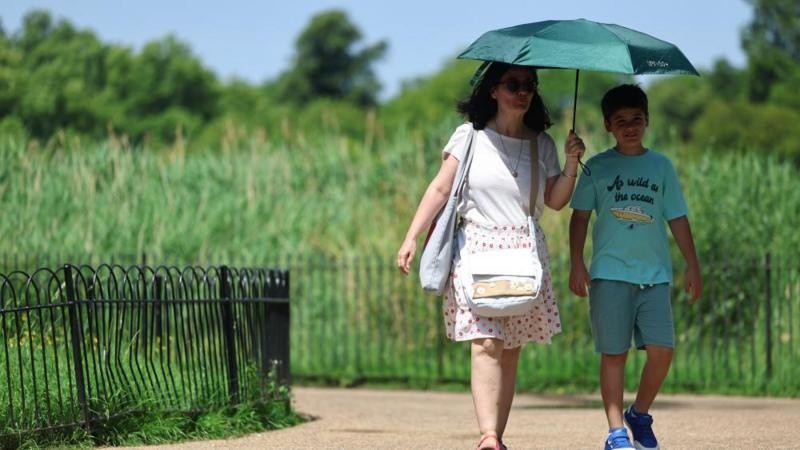 A woman and child using an umbrella to shade from the sun