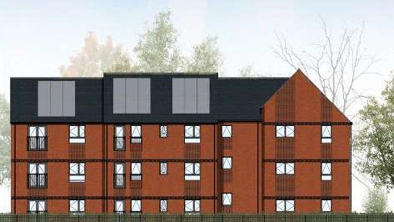 An architect's image of a three-story apartment block with brown brick and a black roof with solar panels on it. There are lots of small windows, and trees in the background