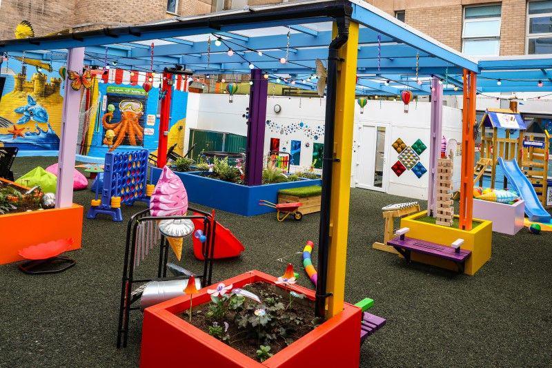 The colourful garden at the hospital. Planters are painted red and blue with murals on the walls. A hard floor has been put down with seating and new windows.