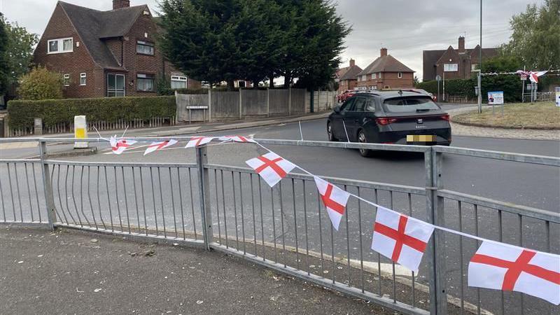 A string of flags on a roundabout. In the background is a black car