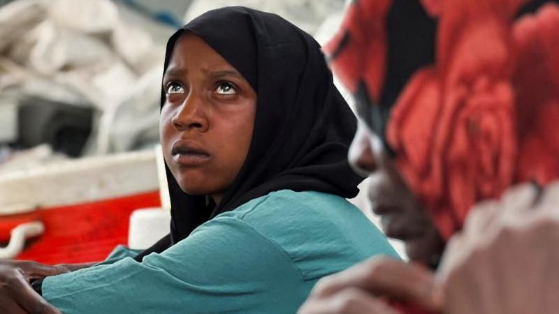 A woman with a scarf wrapped over her head is sitting and staring, with another woman sitting next to her at the Omar ibn al-Khattab displacement site in Kassala state in Sudan on 10 July 2024