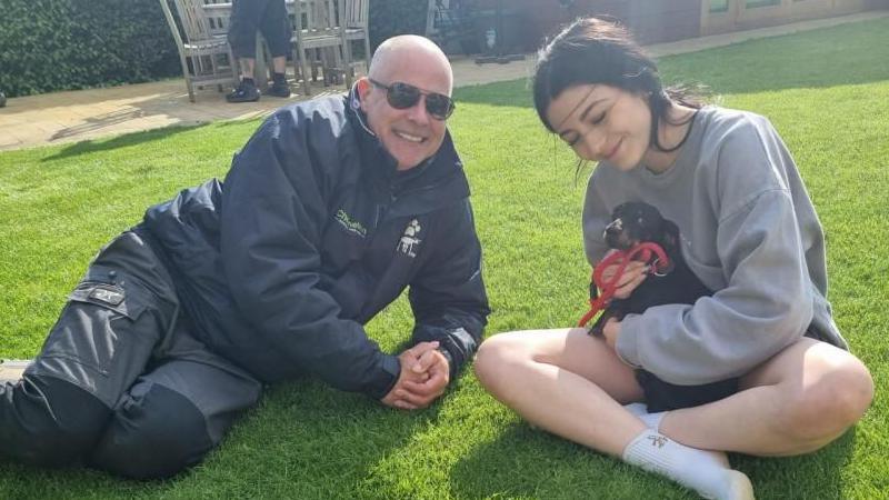 Phil James and Alannah sitting on grass with a dog