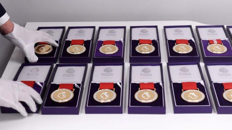 A set of 12 Premier League winners medals sits in cushioned purple display cases while a man wearing white gloves arranges them neatly