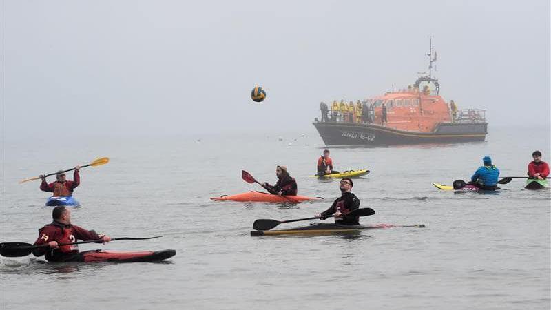 Kayakers playing with their paddles and a football in the sea in Tenby. 