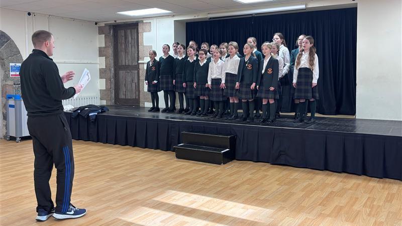 The Melrose choir, which has more than 20 members, singing on stage with their teacher conducting