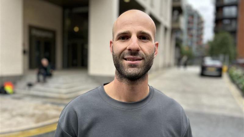 Nikolas Savva, who has a bald head and dark stubble, smiles at the camera wearing a grey jumper.