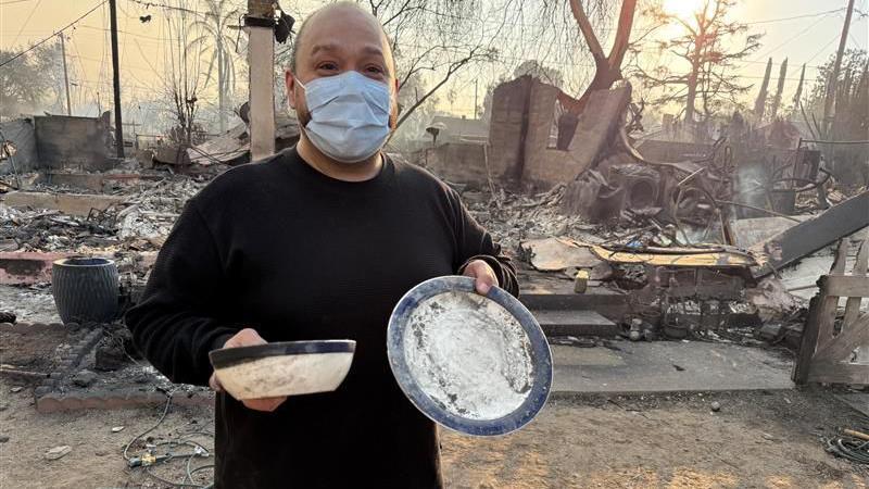 Man in black shirt stands in front of burned-out home