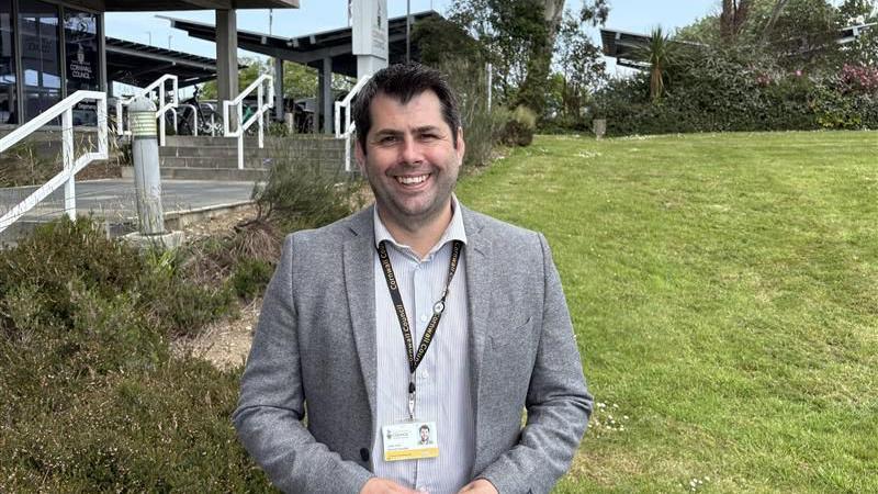 Leigh Frost weaning a suit jacket and shirt smiling in front of the Cornwall Council building