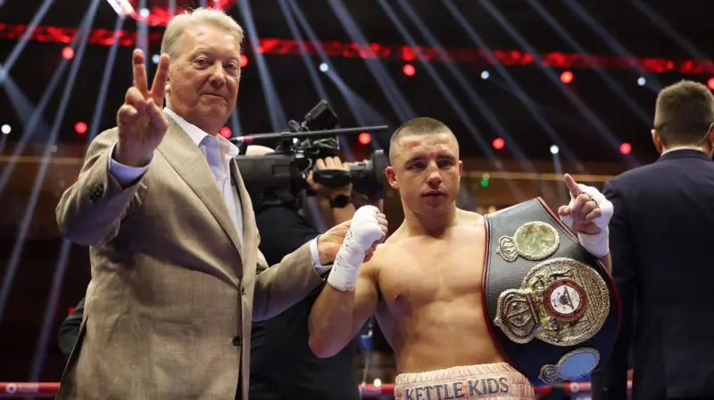 Frank Warren holds up two fingers to the camera beside Nick Ball with his world title