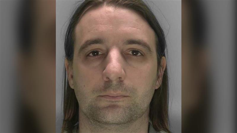 A mug shot of a man with stubble and long, brown hair looking at the camera.