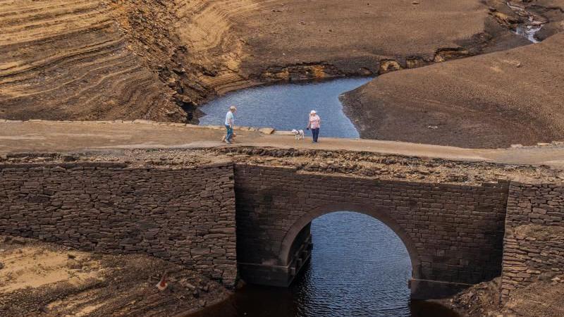 People walk over a bridge that is normally submerged by Baitings Reservoir in Ripponden.