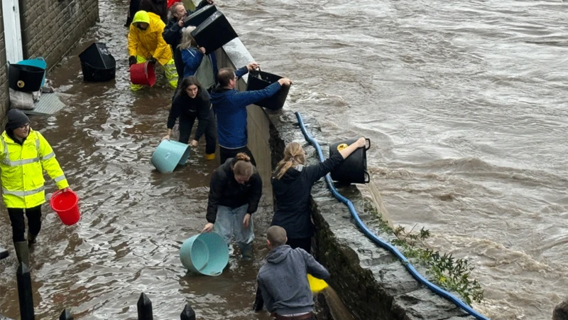 Pobl a bwcedi yn ceisio cael gwared ar ddwr sydd wedi goddiweddid llifglawdd ar lan yr afon Taf ym Mhontypridd.