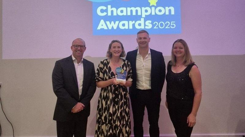 Four people stand in a row as they accept the award. The group are standing in front of a screen which says living wage champions award 2025.