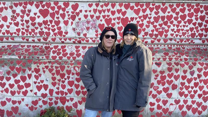 Fran Hall and Lorelei King in front of the memorial wall, both wearing dark coats and Ms Hall wearing sunglasses