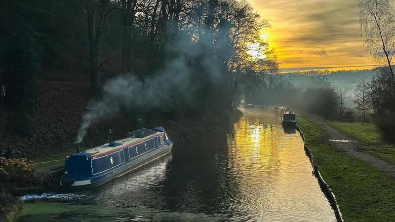 A river with a houseboat on and the sun setting