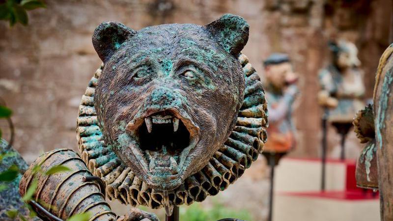 A bust of a bear's head in a ruff in an outdoor area with other similar items in the background
