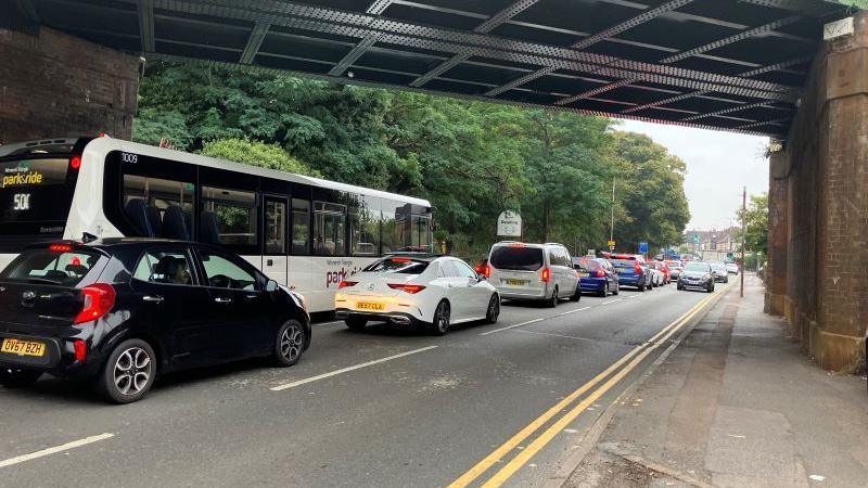 Cars and bus queuing under a railway bridge 