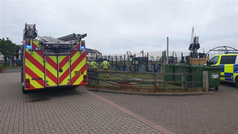 A fire engine and a police van are parked outside a play park named 'Shiver Me Timbers' in Maryport. Firefighters are waiting outside the fencing of the play park.