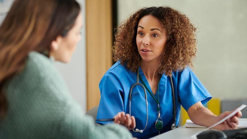 Nurse in blue uniform discusses a test result on a laptop with a patient