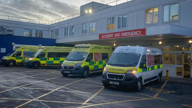 Four ambulances parked outside a white glass panelled building with a red "accident and emergency" sign. 