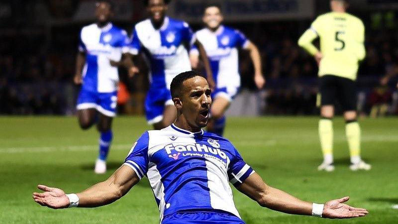 Bristol Rovers player Scott Sinclair slides on his knees in celebration after scoring against Charlton Athletic at the Memorial Stadium. In the background three of his team-mates can be seen running towards him to join in the celebrations